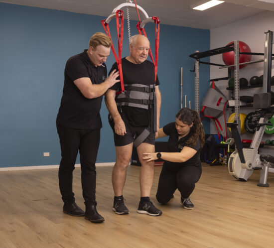 Neuro hoist mature male being assisted by an exercise physiologist and physiotherapist